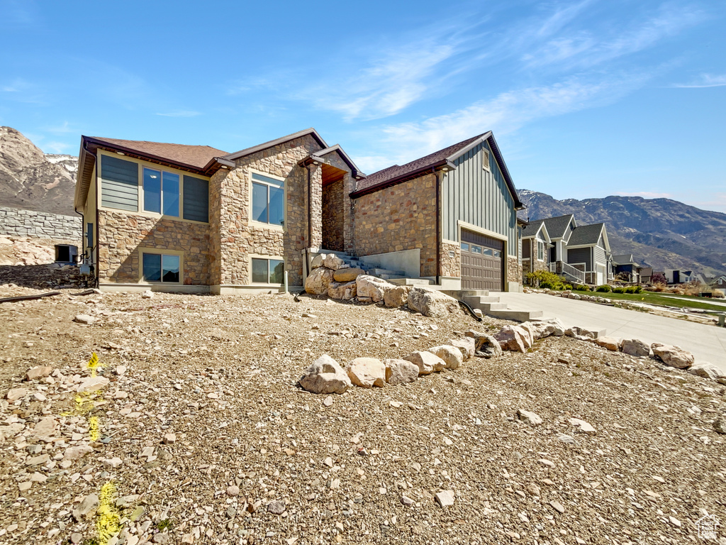 Exterior space with board and batten siding, stone siding, an attached garage, a mountain view, and driveway