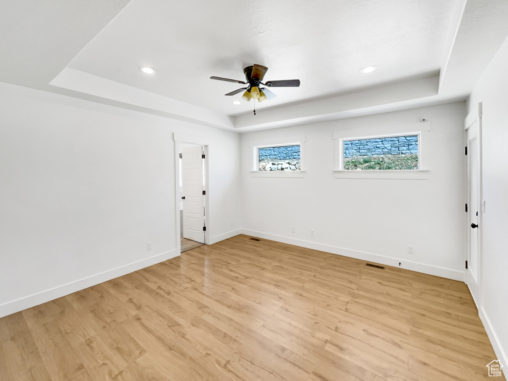 Empty room featuring a tray ceiling, ceiling fan, and light wood finished floors