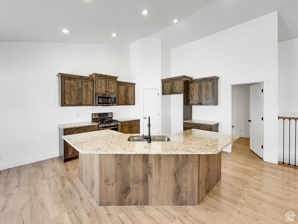 Kitchen featuring a sink, appliances with stainless steel finishes, a large island with sink, high vaulted ceiling, and light stone counters