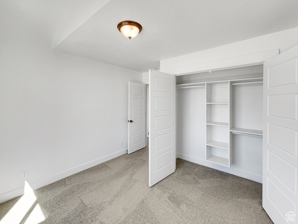 Unfurnished bedroom with light carpet, baseboards, and a closet