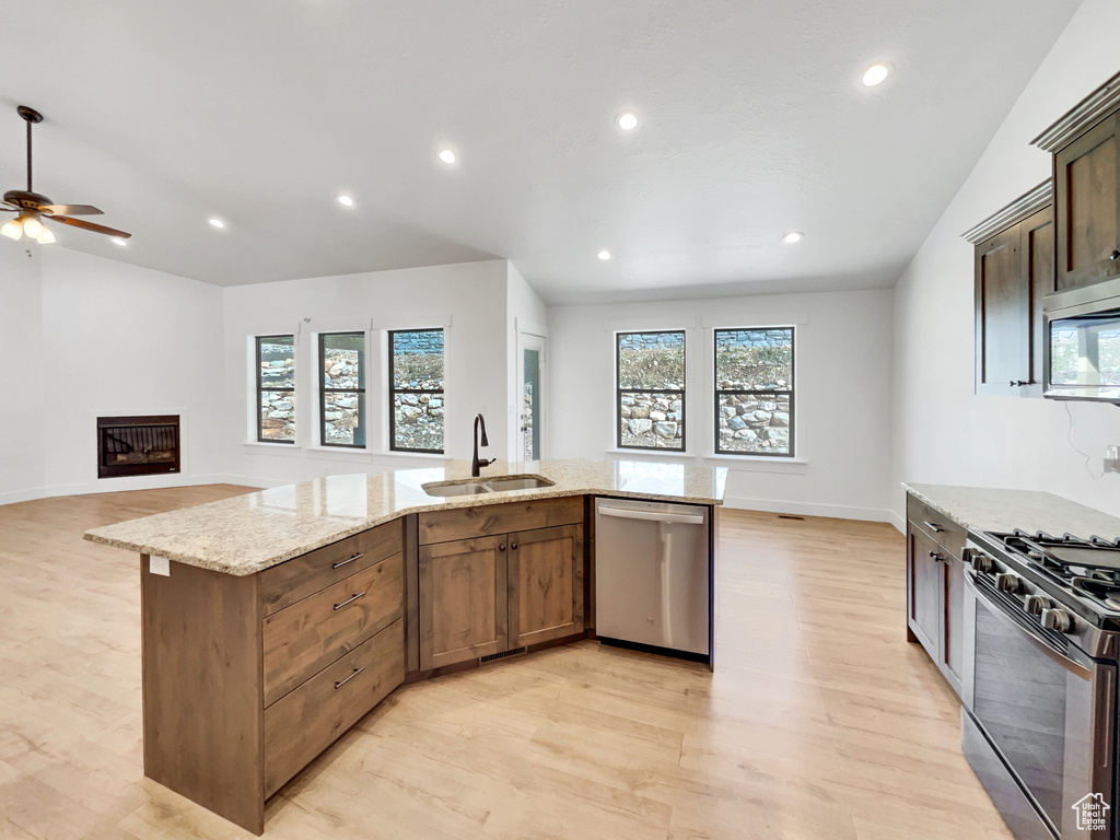 Kitchen featuring light wood-style floors, ceiling fan, light stone counters, a sink, and stainless steel appliances