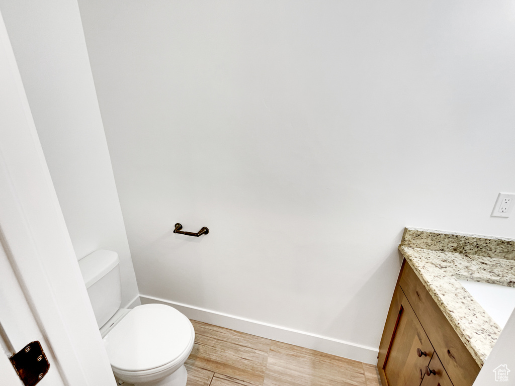 Half bath with toilet, wood finished floors, vanity, and baseboards