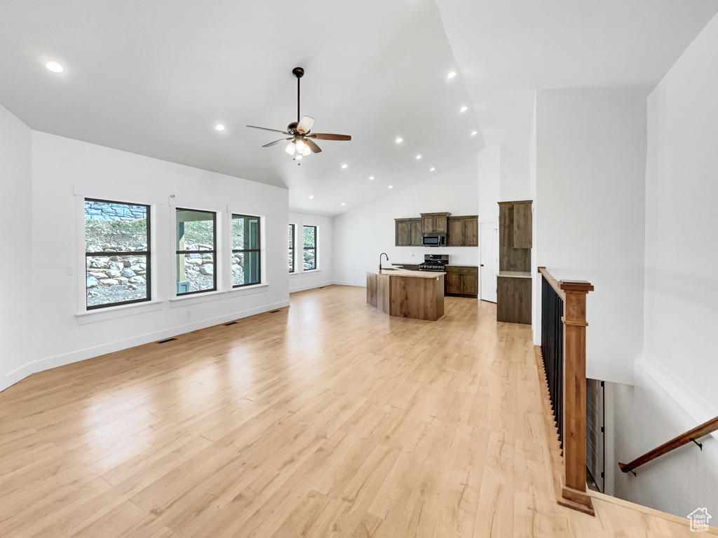 Unfurnished living room with light wood-style floors, high vaulted ceiling, a ceiling fan, recessed lighting, and a sink