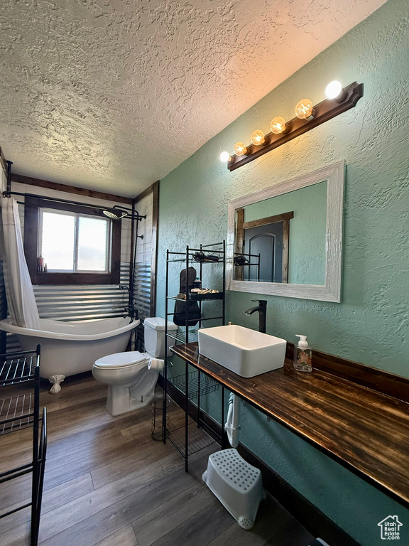Full bath featuring a textured wall, a textured ceiling, a soaking tub, toilet, and wood finished floors