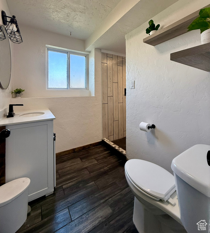 Bathroom with toilet, vanity, a textured wall, a textured ceiling, and wood finished floors