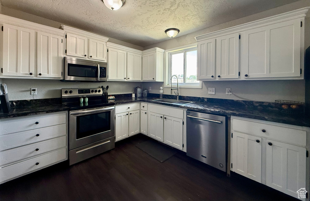 Kitchen with appliances with stainless steel finishes, a sink, white cabinetry, dark wood-type flooring, and a textured ceiling