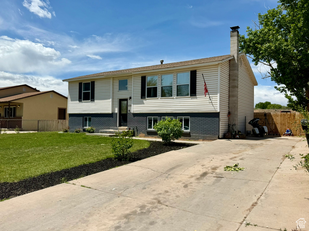 Raised ranch with a chimney, brick siding, and concrete driveway