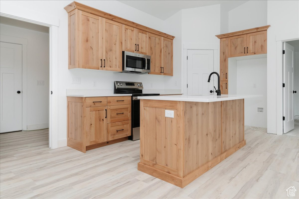Kitchen featuring stainless steel appliances, light wood-style floors, light countertops, and a center island with sink