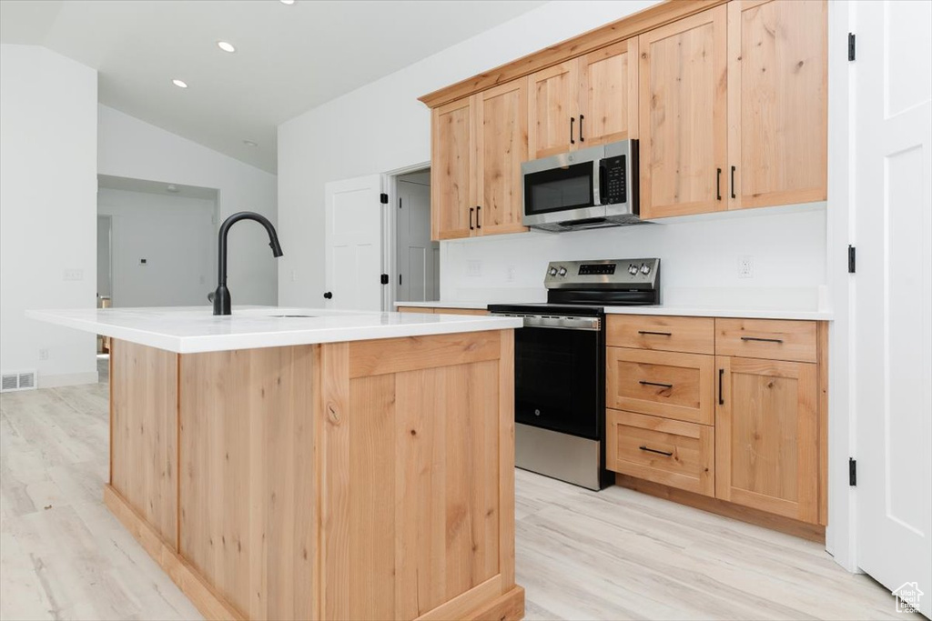Kitchen featuring light wood-style flooring, appliances with stainless steel finishes, light brown cabinets, and lofted ceiling