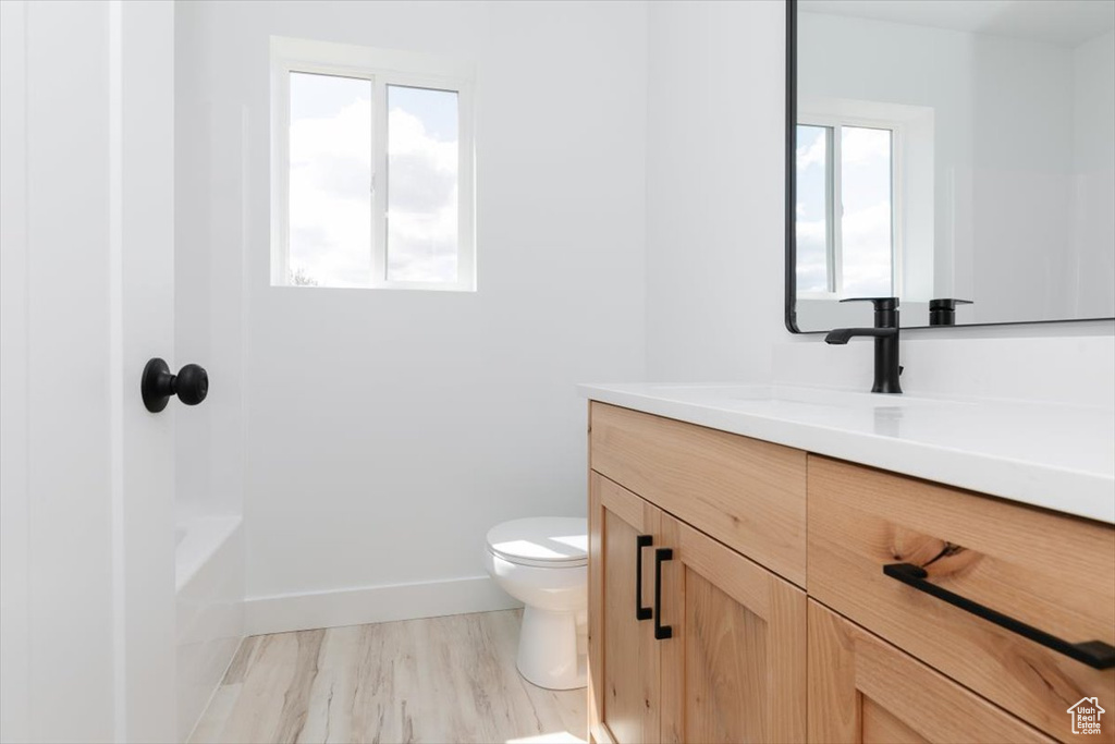 Full bathroom with toilet, vanity, wood finished floors, and a wealth of natural light