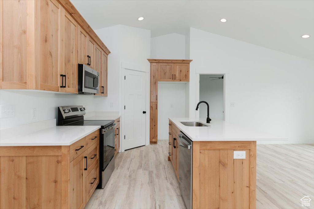 Kitchen featuring light wood-style flooring, light countertops, a center island with sink, appliances with stainless steel finishes, and a sink