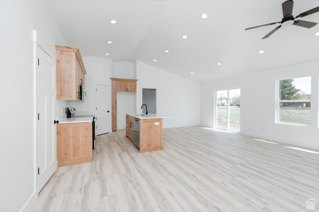 Kitchen with lofted ceiling, light brown cabinetry, stainless steel appliances, light countertops, and open floor plan