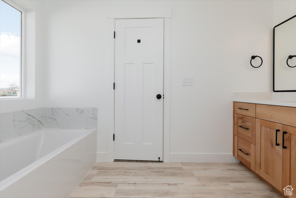 Full bathroom featuring a bath, baseboards, wood finished floors, and vanity