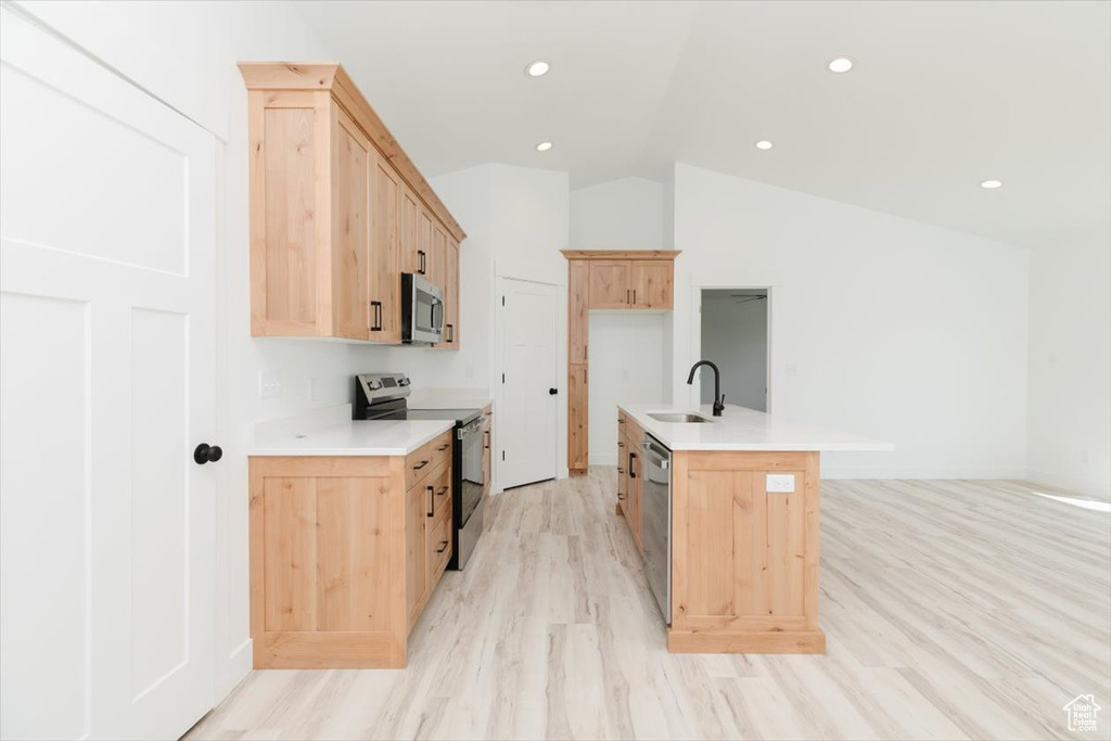Kitchen featuring lofted ceiling, light brown cabinets, a sink, light wood-style flooring, and appliances with stainless steel finishes