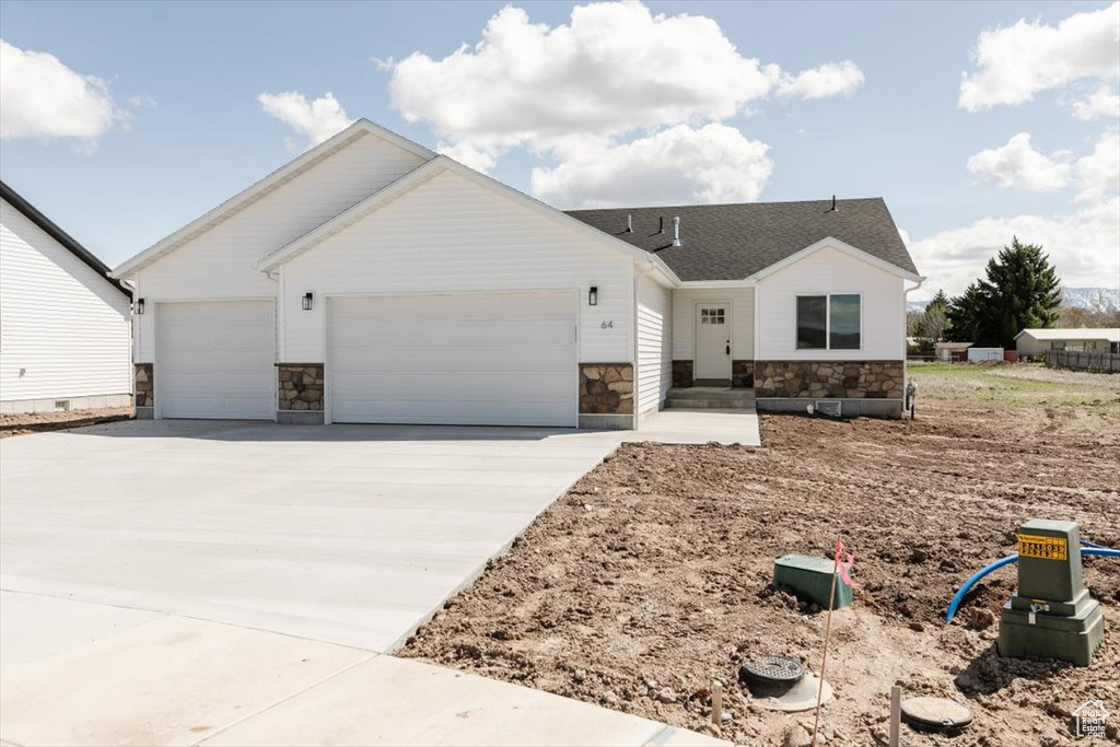 Ranch-style home with driveway, stone siding, and a garage