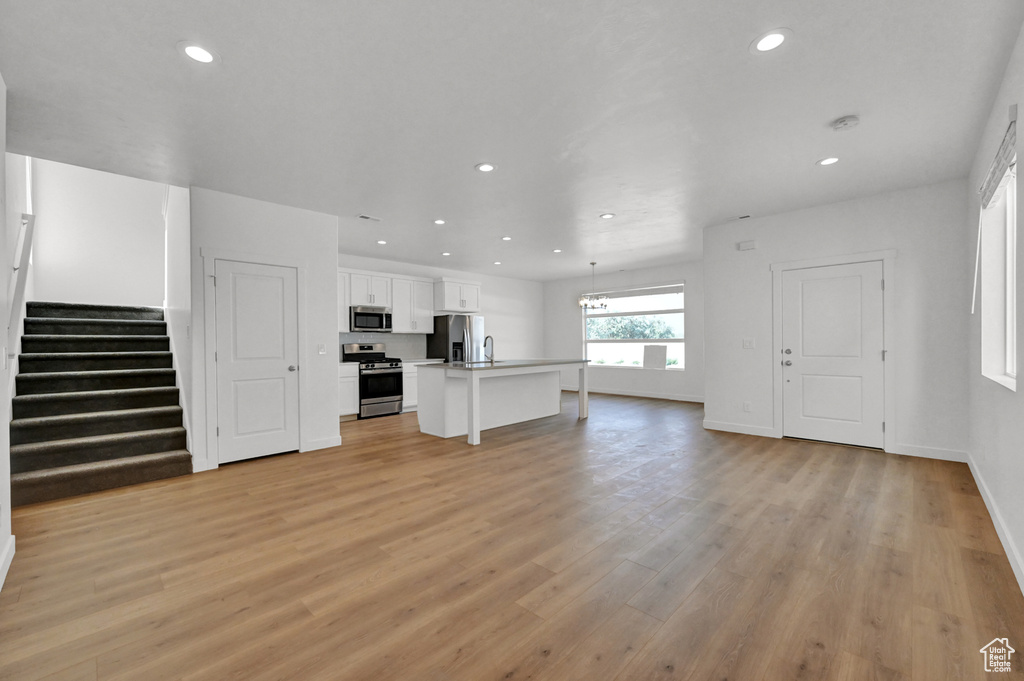 Unfurnished living room featuring light wood-style flooring, recessed lighting, baseboards, and stairs