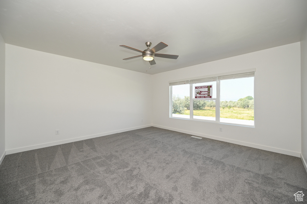 Empty room with ceiling fan, baseboards, visible vents, and dark colored carpet