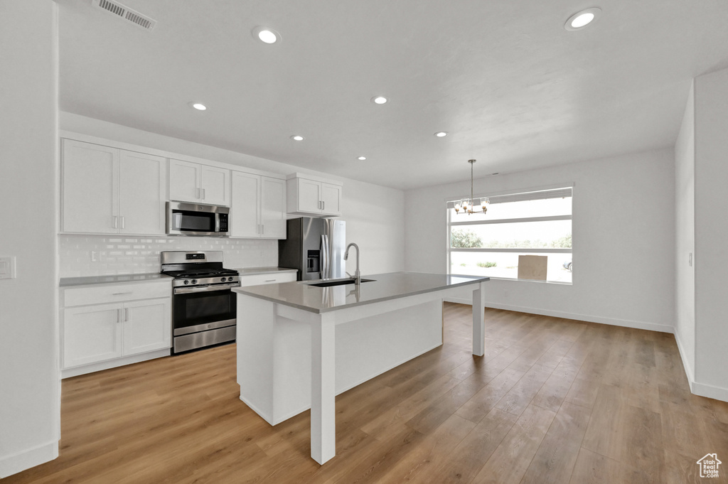 Kitchen featuring an island with sink, white cabinets, visible vents, appliances with stainless steel finishes, and a sink