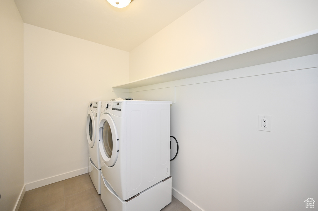 Washroom with independent washer and dryer, light tile patterned flooring, laundry area, and baseboards