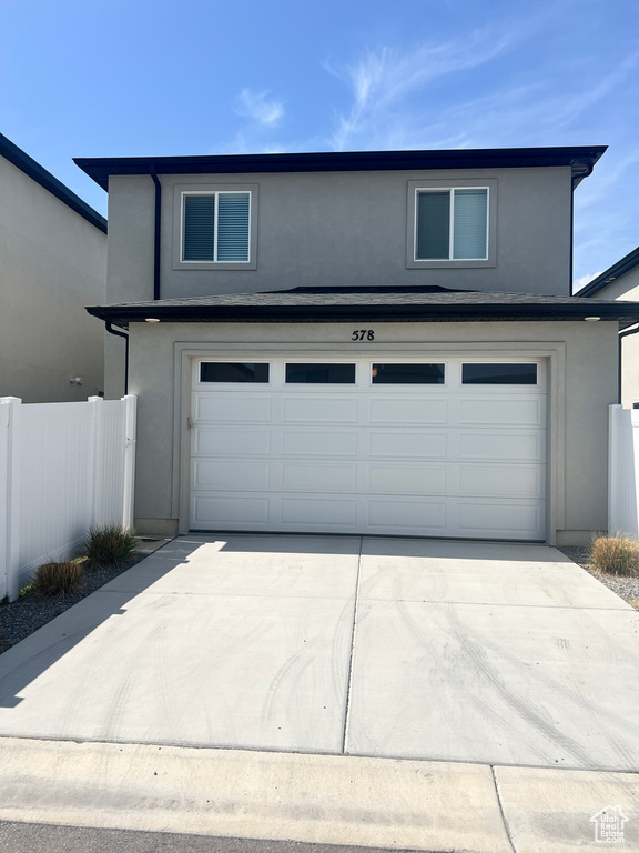 View of front facade with a garage, stucco siding, fence, and concrete driveway