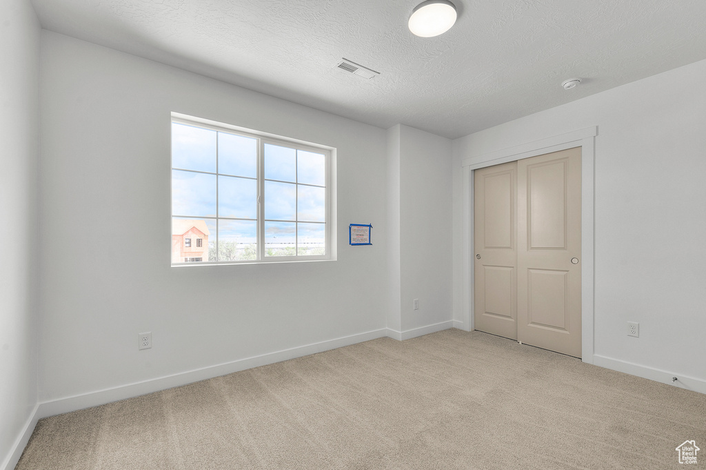 Unfurnished bedroom featuring light colored carpet, baseboards, a textured ceiling, and a closet