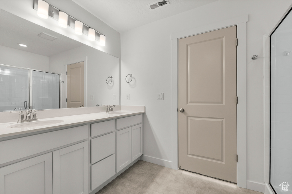 Bathroom featuring a stall shower, double vanity, and baseboards