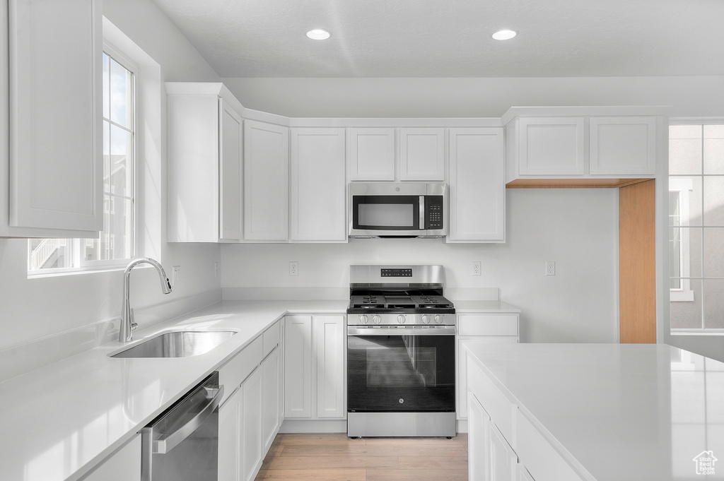 Kitchen featuring appliances with stainless steel finishes, a sink, white cabinets, light countertops, and recessed lighting
