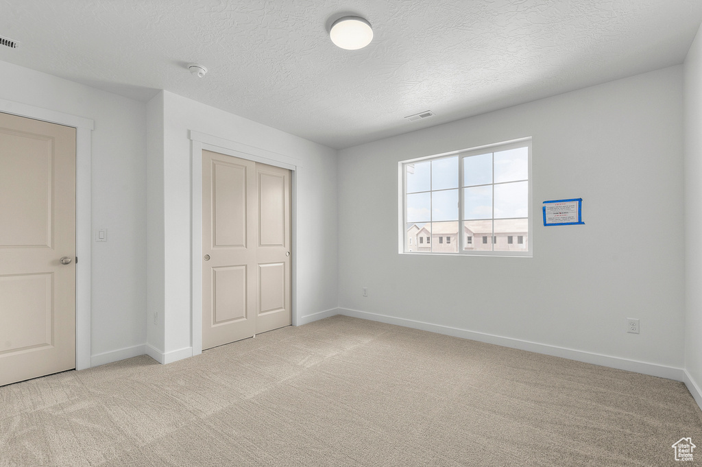 Unfurnished bedroom with light carpet, baseboards, a textured ceiling, and a closet