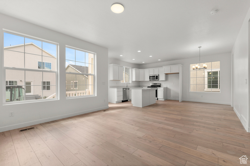 Kitchen featuring appliances with stainless steel finishes, a chandelier, baseboards, white cabinetry, and open floor plan