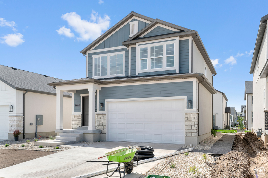View of front facade featuring a garage, concrete driveway, stone siding, and board and batten siding