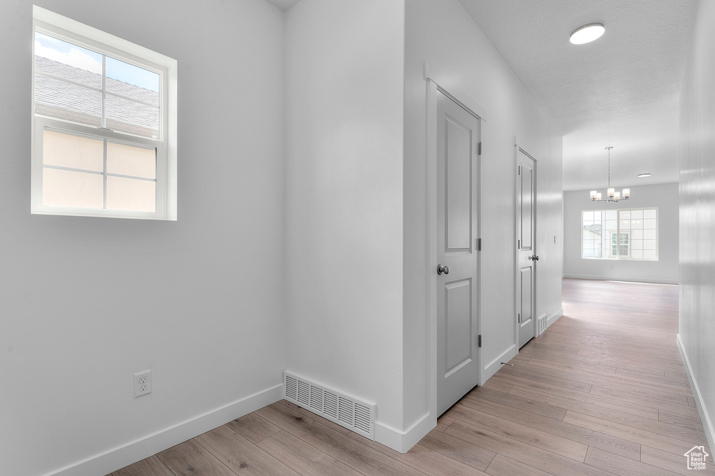 Hall featuring baseboards, a chandelier, and light wood-style floors
