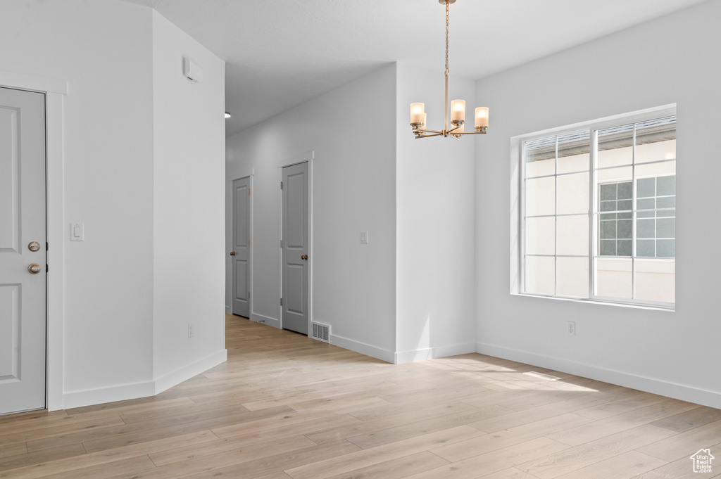 Spare room with a chandelier, light wood-style floors, and baseboards