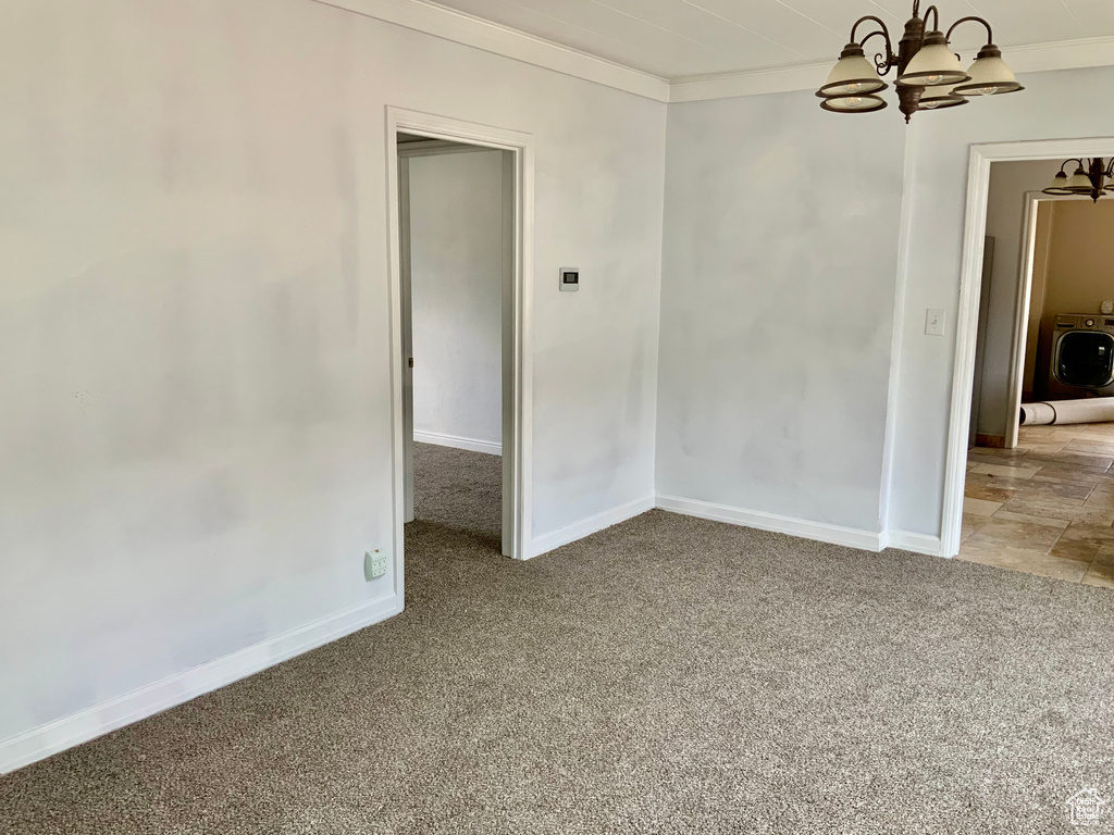 Carpeted empty room with crown molding, washer / clothes dryer, baseboards, and a notable chandelier