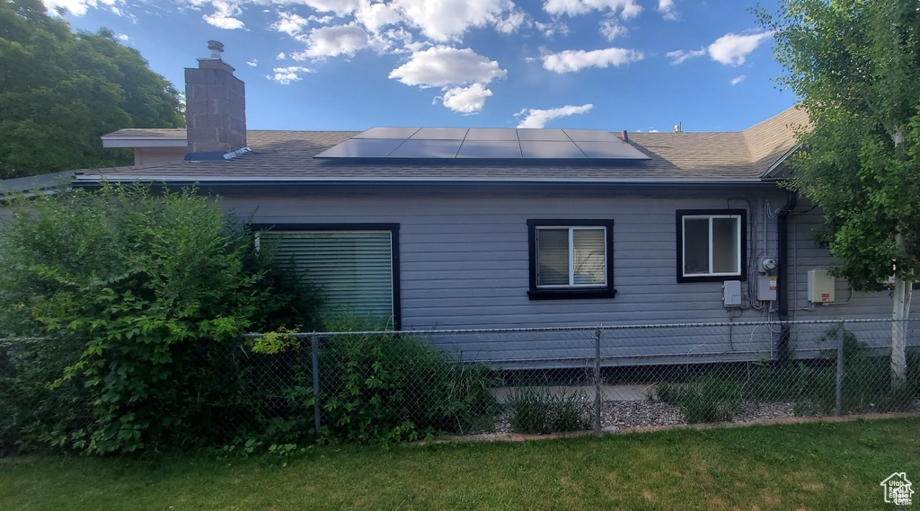 View of side of property with a chimney, a shingled roof, fence, a lawn, and roof mounted solar panels