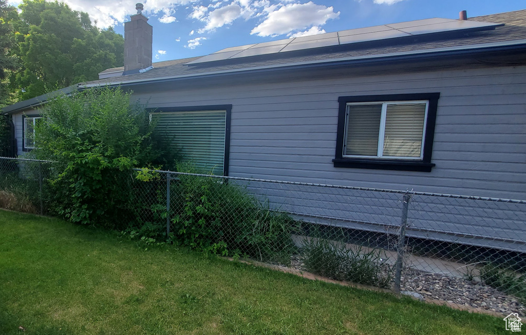 View of side of property with a chimney, fence, a lawn, and roof mounted solar panels