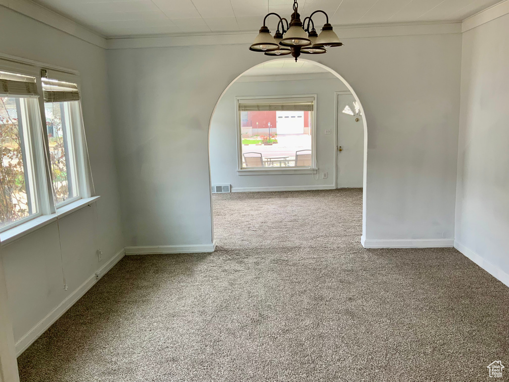 Carpeted spare room with a chandelier, arched walkways, visible vents, and crown molding