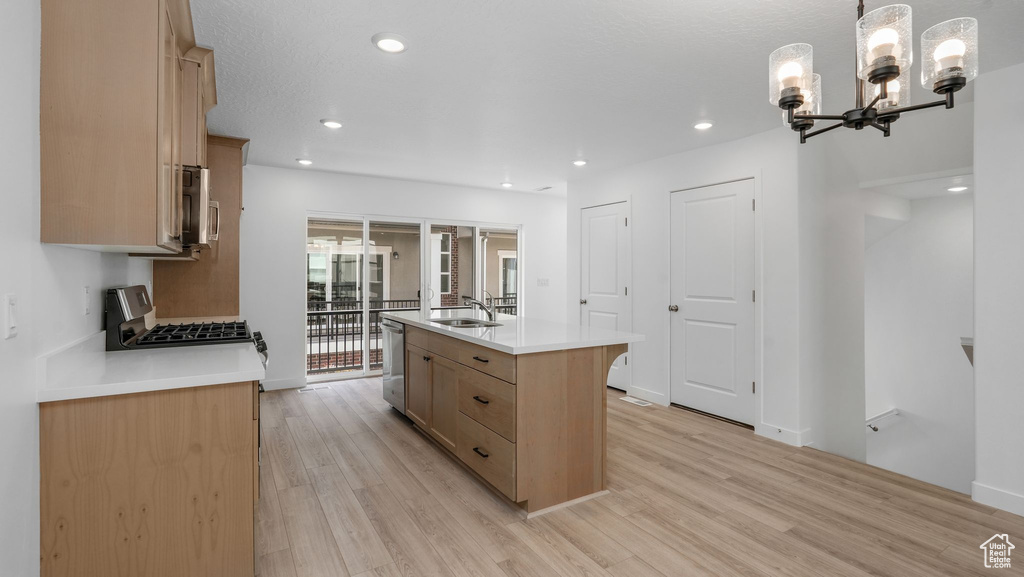 Kitchen featuring light wood-style flooring, appliances with stainless steel finishes, a kitchen island with sink, light countertops, and a chandelier