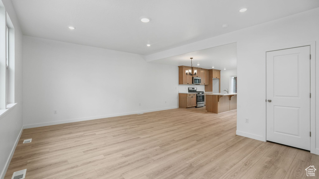 Unfurnished living room with a chandelier, light wood finished floors, and recessed lighting