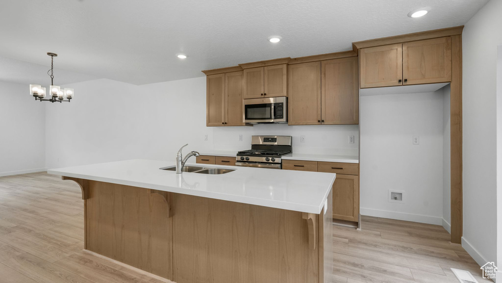 Kitchen featuring appliances with stainless steel finishes, light wood-style flooring, a chandelier, light countertops, and decorative light fixtures