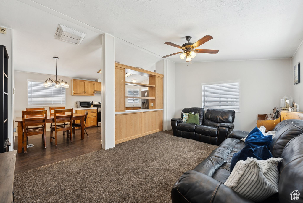 Living area with ceiling fan with notable chandelier and dark carpet