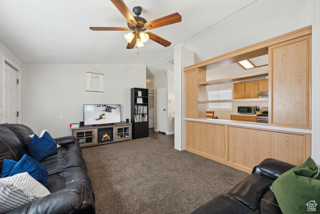 Living area featuring dark colored carpet, vaulted ceiling, and a ceiling fan