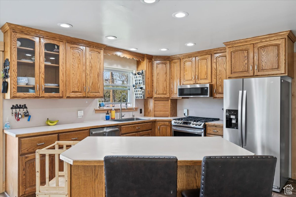 Kitchen with glass insert cabinets, a sink, light countertops, recessed lighting, and stainless steel appliances