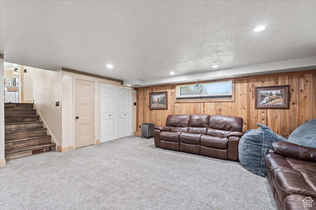 Carpeted living room featuring wood walls, baseboards, recessed lighting, and stairway