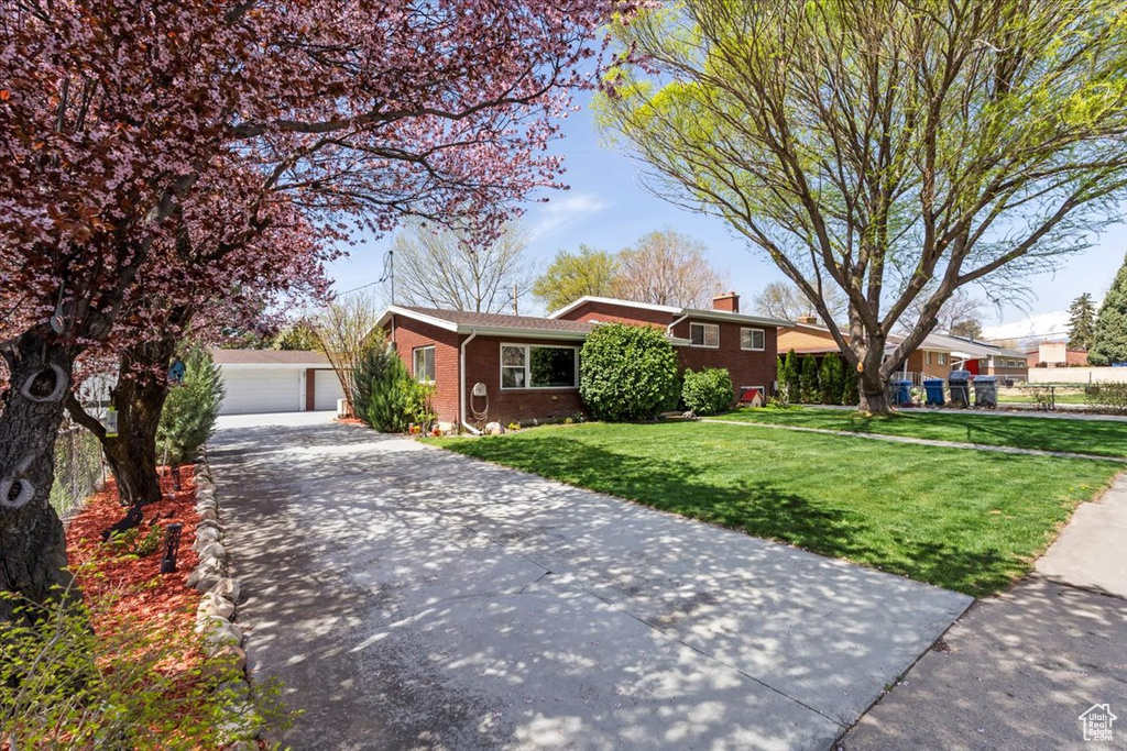 View of front of home featuring an outdoor structure, a chimney, a detached garage, a front yard, and brick siding