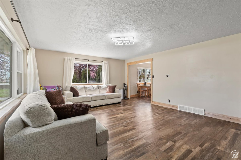 Living area featuring visible vents, baseboards, a textured ceiling, and wood finished floors