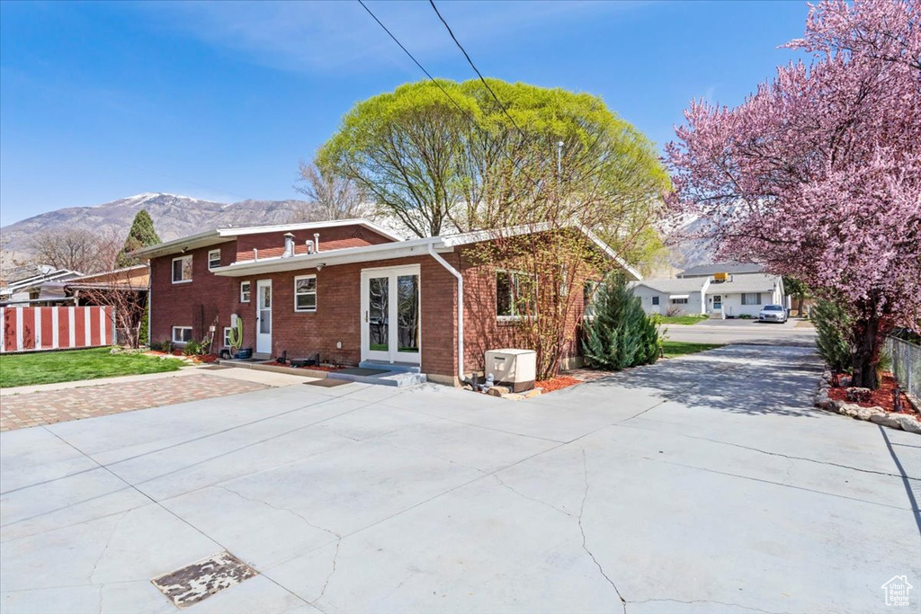 Back of property featuring a mountain view, french doors, brick siding, fence, and a lawn