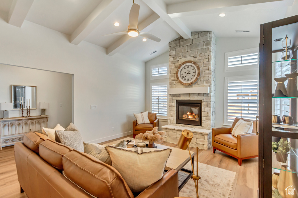 Living room featuring baseboards, a ceiling fan, a fireplace, light wood finished floors, and vaulted ceiling with beams