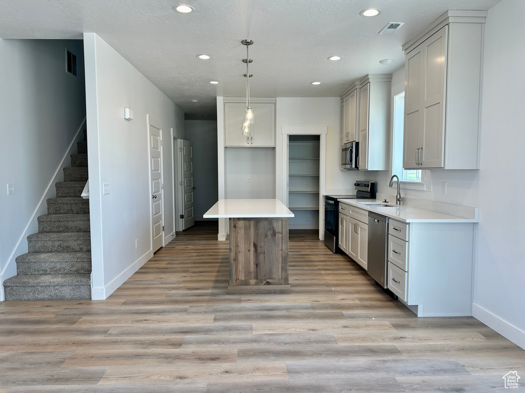 Kitchen featuring appliances with stainless steel finishes, recessed lighting, light wood-style floors, light countertops, and pendant lighting