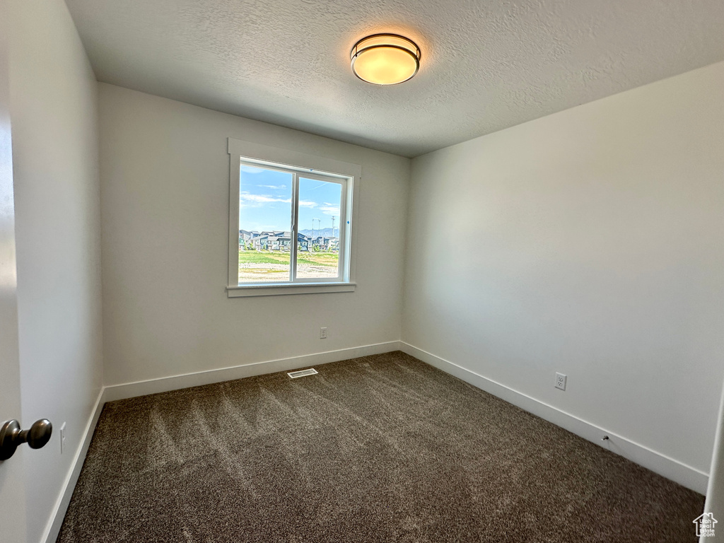 Unfurnished room featuring dark colored carpet and a textured ceiling