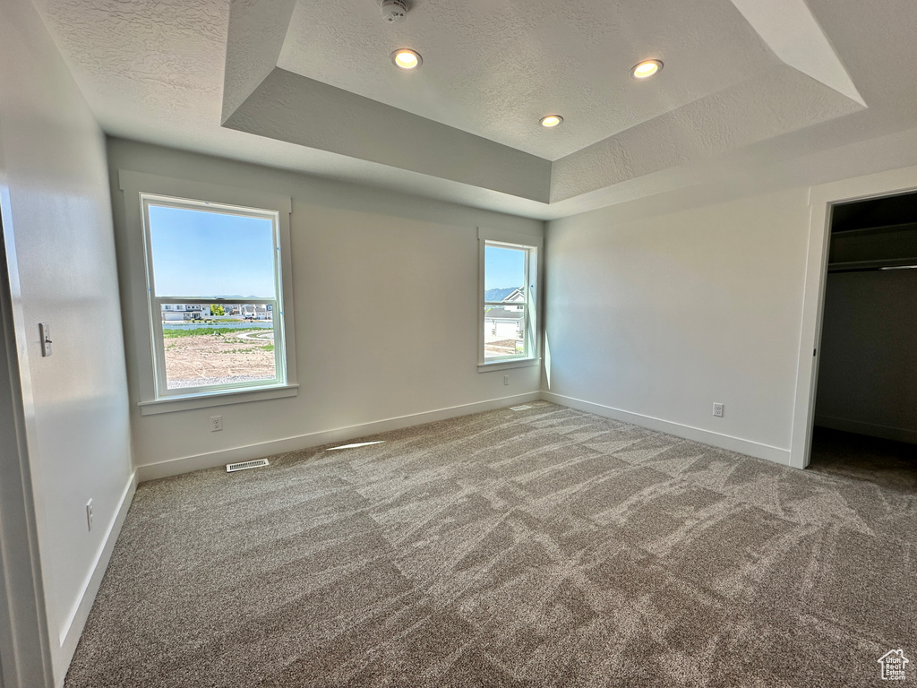 Unfurnished bedroom featuring a tray ceiling, a textured ceiling, carpet floors, recessed lighting, and a walk in closet